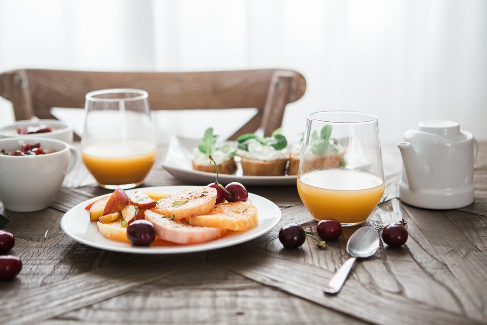 A breakfast with fruits, orange juice and bread with cream on a wooden table